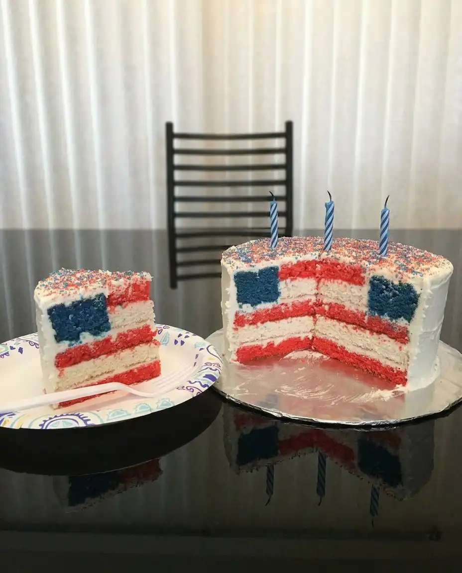 A slice of flag cake served on a plate with fresh strawberries and blueberries.