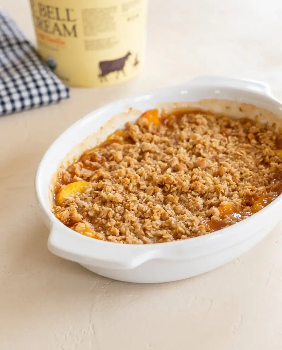 A bowl of warm Peach Crisp topped with a melting scoop of vanilla ice cream.