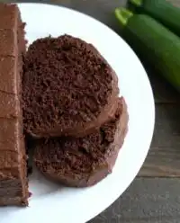 A moist Chocolate Lover’s Zucchini Cake with rich chocolate frosting on a white plate
