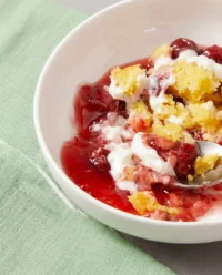 A warm serving of Strawberry Cheesecake Dump Cake in a bowl with whipped cream