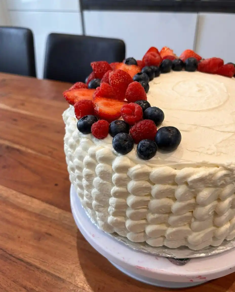 A generous slice of Patriotic Berry Cake on a white plate showing the red and blue fruit filling layers.