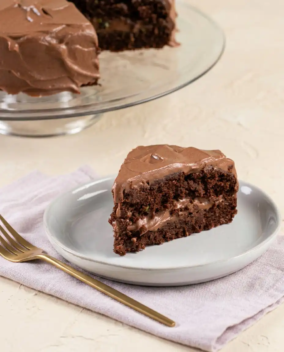 Dairy-Free Chocolate Zucchini Cake 16 A square of dairy-free chocolate zucchini cake served on a plain plate with a cup of black coffee.
