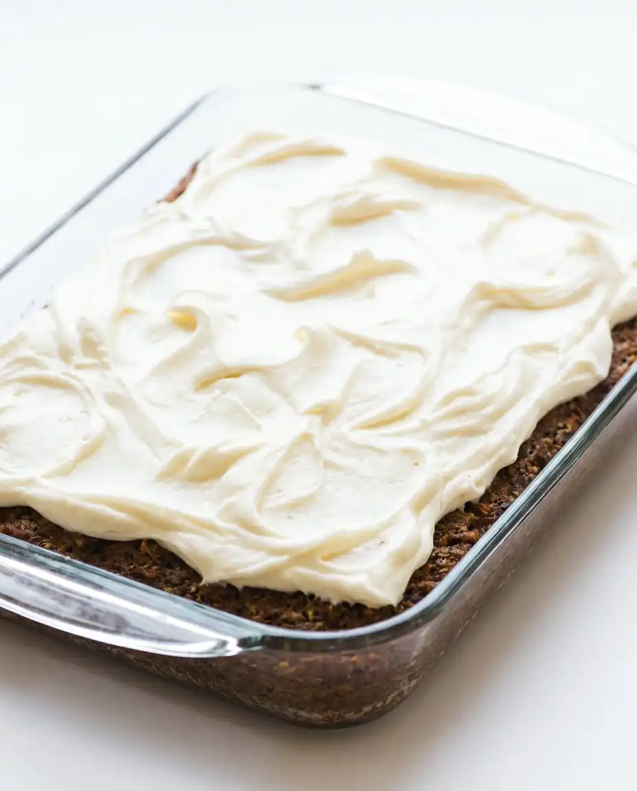A thick slice of Old-Fashioned Zucchini Cake topped with white cream cheese frosting on a plate.