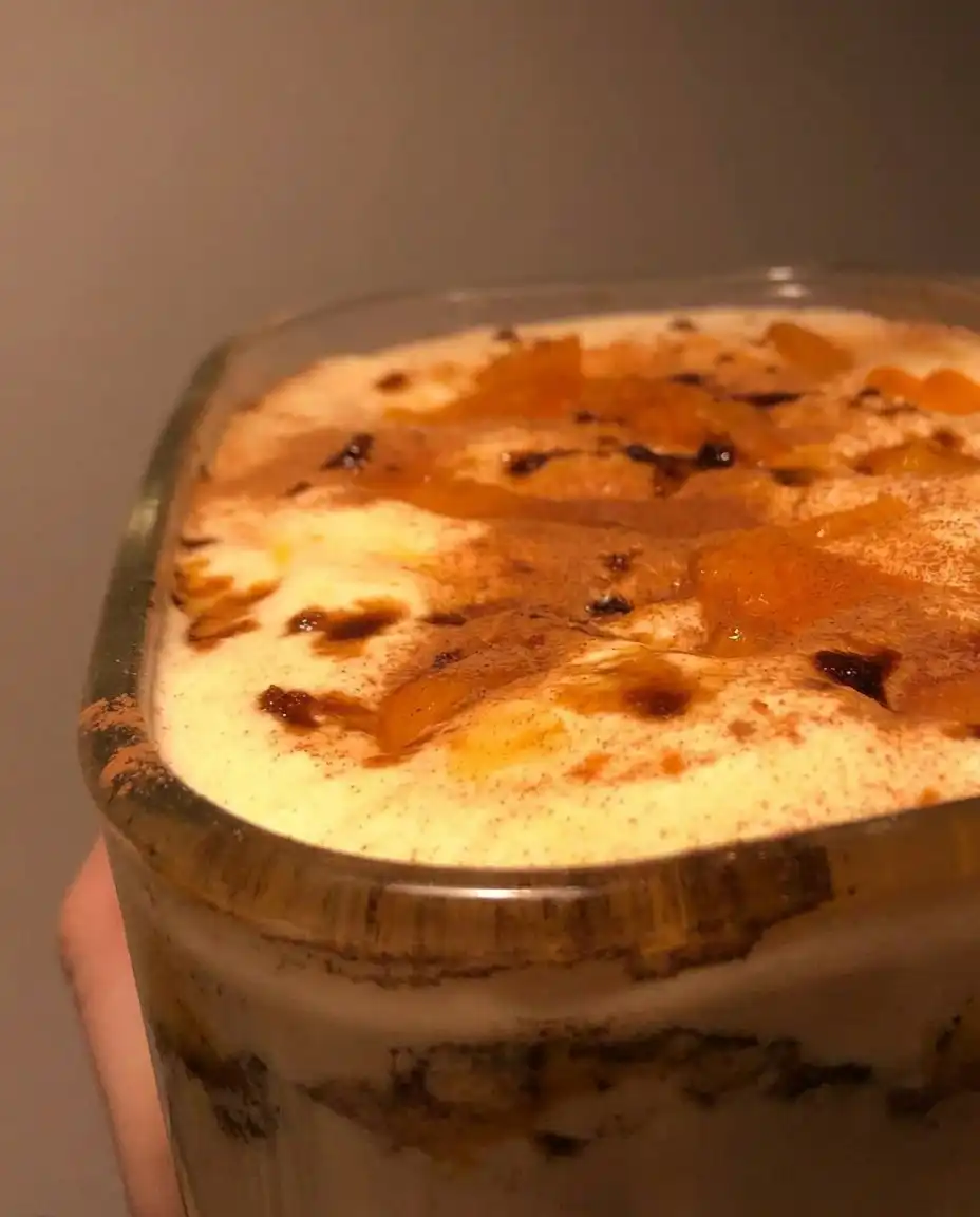 A square slice of peach tiramisu on a white plate with peach compote