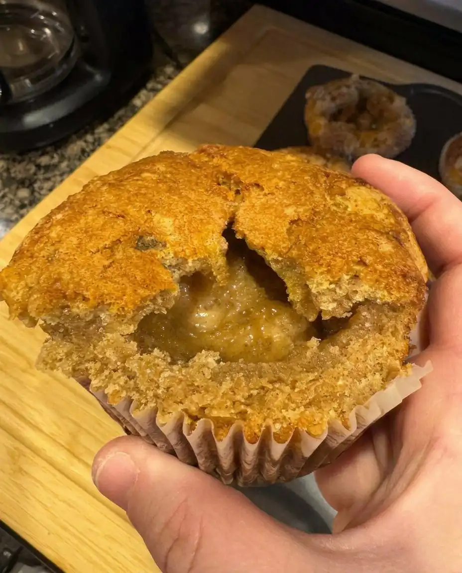 A hand sprinkling cinnamon sugar over muffin batter in a tin