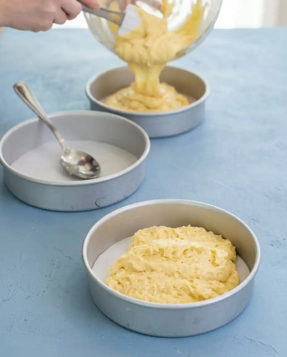 A spatula folding purple blackberry preserves into white lemon frosting for a Blackberry Lemon Cake.
