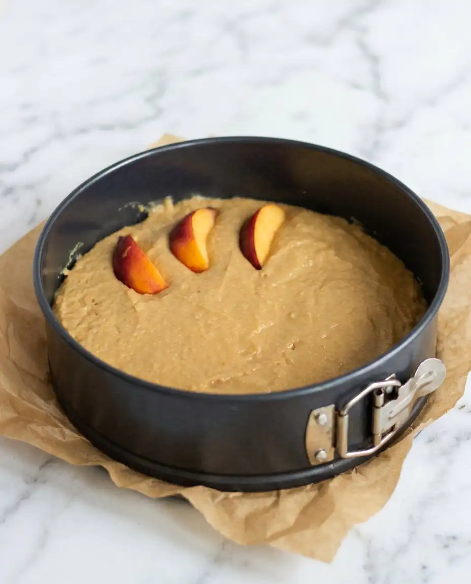 A baker spreading thick batter for a Sour Cream Peach Coffee Cake into a prepared pan.