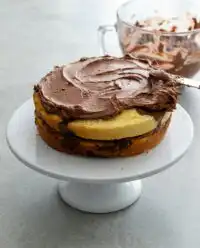 A beautiful Two-Layer Marble Cake sitting on a wooden kitchen counter under a glass dome.