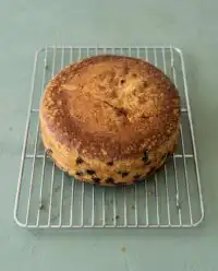 A golden brown blueberry lemon olive oil cake resting on a cooling rack with fresh blueberries around it.
