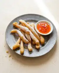 Crispy golden classic funnel cake fries dusted with powdered sugar in a paper cone