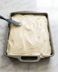 A golden brown Pumpkin Spice Cake cooling in a worn metal nine by thirteen baking pan on a wire rack.