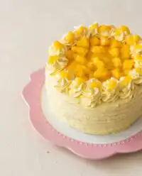 A beautiful homemade Mango Ombre Cake frosted with light orange whipped cream on a vintage cake stand.