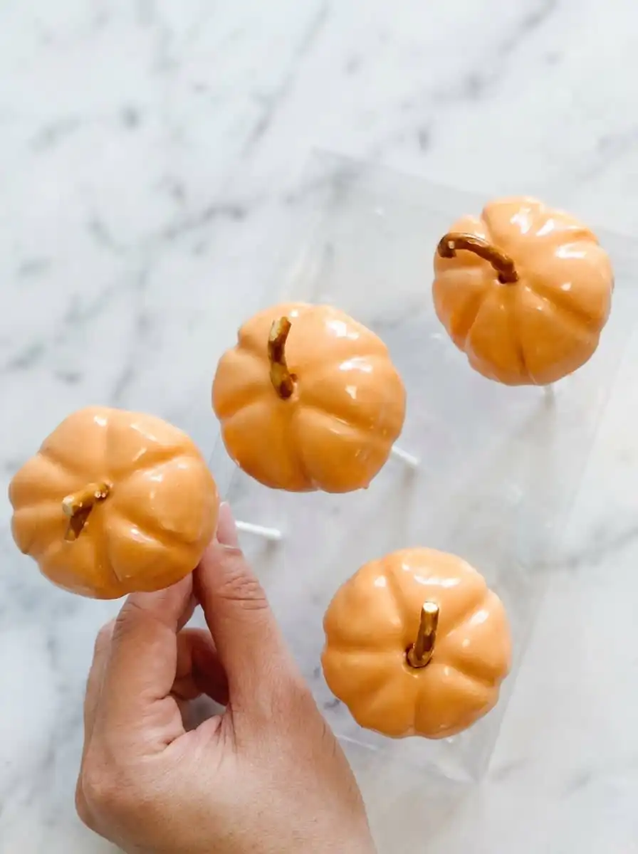 Classic Pumpkin Cake Pops 12 A stack of delicious Classic Pumpkin Cake Pops decorated with green vines on a wooden plate.