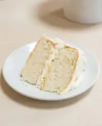 A beautiful Two-Layer Buttermilk Cake topped with smooth vanilla frosting on a white stand.