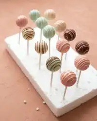 A close up view of classic vanilla cake pops decorated with white coating and sprinkles on a tray.