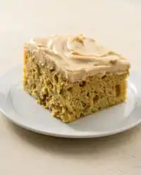 A freshly baked square zucchini cake with cinnamon and nutmeg topped with rich cream cheese icing and walnuts.