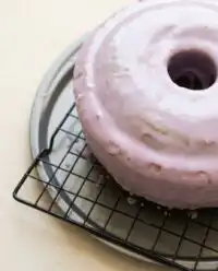 A gorgeous homemade Blackberry Pound Cake topped with a sweet pink glaze on a white cake stand.
