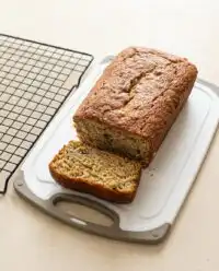 A freshly baked golden brown loaf of cake mix banana bread resting on a wire cooling rack.