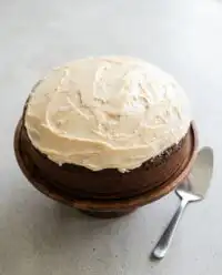 A beautiful moist Marzipan Carrot Topped Cake on a rustic wooden platter decorated with cream cheese frosting.