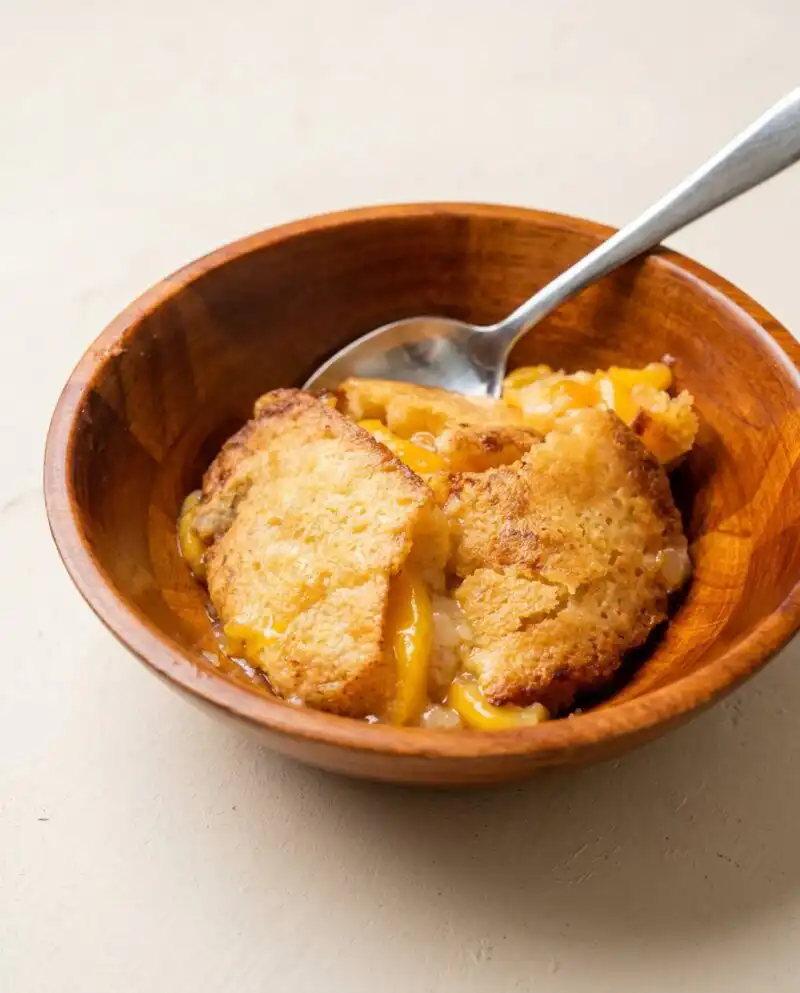 A golden brown slice of Peach Cobbler Sheet Cake topped with fresh peach slices and crumble