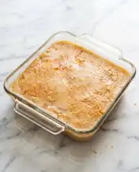 A warm peach dump cake with frozen peaches in a ceramic baking dish, topped with toasted pecans and melted butter