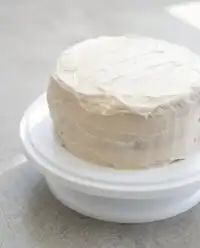 A rustic Pumpkin Spice Layer Cake with Cinnamon Cream Cheese Frosting sliced on a ceramic white serving platter.