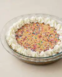 A beautiful whole Rainbow Sprinkle Cookie Cake decorated with vanilla buttercream frosting and colorful jimmies.