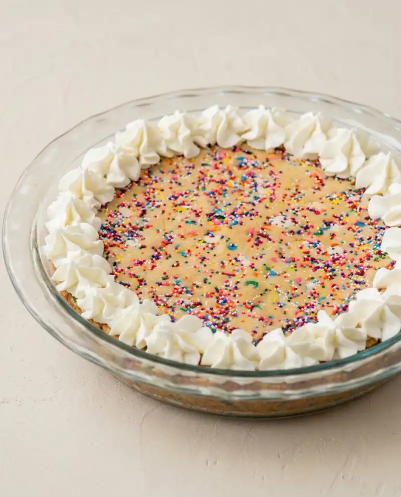 A beautiful whole Rainbow Sprinkle Cookie Cake decorated with vanilla buttercream frosting and colorful jimmies.