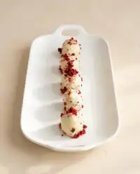 A gorgeous platter of glossy white Red Velvet Cake Pops with bright red drizzles.