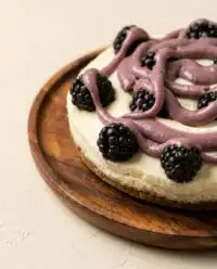 A rustic layered Blackberry Vanilla Cake sitting on a vintage stand in a sunny farmhouse kitchen.