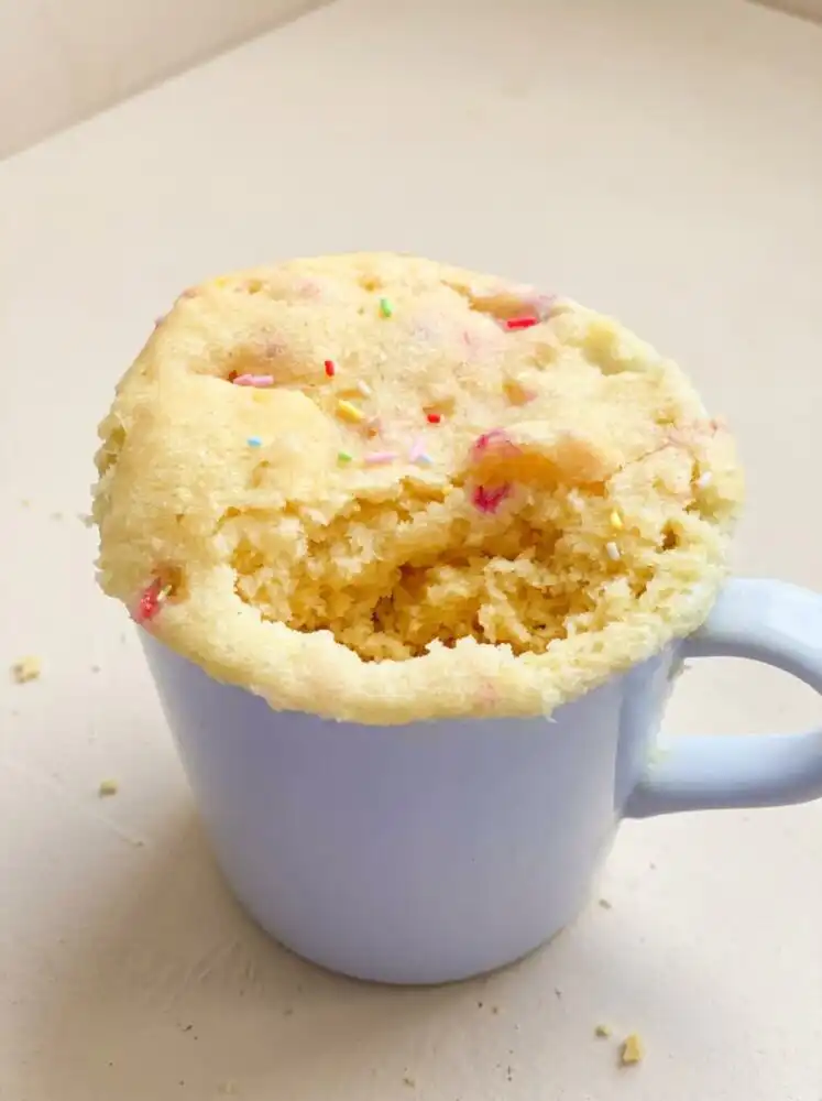 Home - Cake Savor - Savor the Simple 1 A warm steaming 1-Minute Vanilla Mug Cake in a white ceramic mug with colorful rainbow sprinkles on top