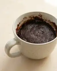 A warm chocolate mug cake topped with whipped cream inside a blue ceramic mug on a wooden table.