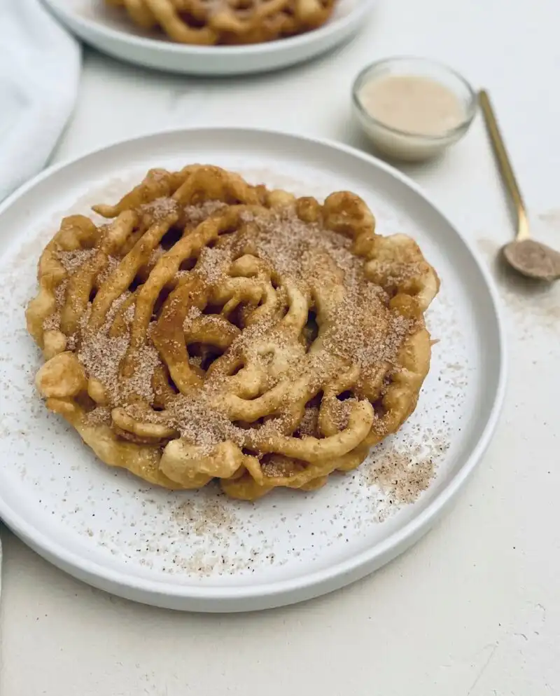 A high-angle shot of warm Cinnamon Sugar Funnel Cake Bites served in a nostalgic paper cone.